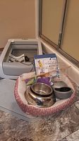 Wide view of Petsafe self-cleaning litter box next to cat bed with feeding bowls and toys inside