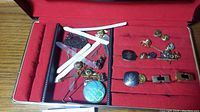 Jewelry case containing men's accessories including cufflinks, pins, lapel pins, tie clips, collar stays and other small items arranged on red velvet lining.