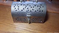 Side/top angled view of the vintage brass box showing floral cutout pattern, handle, and locking latch on front