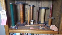 Wide view of seven vintage wooden textile spools arranged on a wooden shelf with small accompanying items including a coral-like rock and thread bundle.