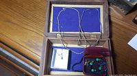 Wooden jewelry box showing two necklaces, a small white box with drop earrings inside, and a maroon velvet box with a beaded bracelet and gold-tone earrings.
