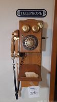 Vintage wooden wall phone with rotary dial, brass bells, handset, and lucky rabbit foot on shelf below.