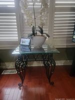 Glass end table with clear square glass top and decorative black metal curved legs and apron.