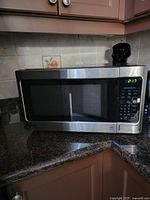 Front angled view of LG microwave oven on kitchen countertop showing stainless steel exterior, black window, and control panel with digital clock display