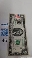 Photo of a 1976 US two dollar bill with bicentennial overprint and black stamp, serial number L16859660A.