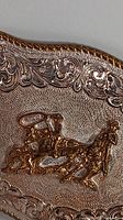 Close-up photo showing detailed cowboy roping calf motif and intricate scrollwork on vintage belt buckle