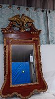 Full view of the ornate wooden-framed wall mirror with gold trim and eagle figure detail at the top.