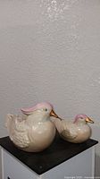 Pair of vintage porcelain bird figurines placed on a black surface against a textured wall.