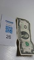 Top view of the 2 dollar bill partially folded with the MaxSold support code next to it.