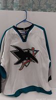 Front view of the white San Jose Sharks jersey with teal and black accents and the team logo on the chest.