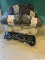 Photo showing several skeins of gray acrylic yarn wrapped in plastic packaging, along with white and navy blue yarn skeins visible.
