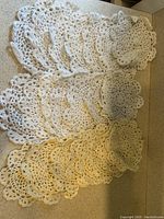 Photo of several white and off-white crocheted doilies laid out in rows showing different sizes and patterns.