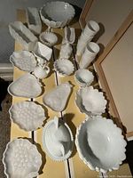 Top view of assorted milk glass collection showing bowls, plates, cups, and decorative pieces on a table surface.