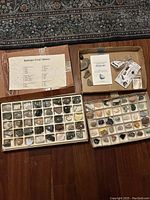 Two closed cardboard boxes with trays of rock and mineral specimens, a few loose minerals, fossils, and paper guides visible on top.