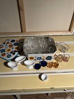 Photo showing various clear, colored, and white ceramic salt cellars arranged near a decorative tin box with floral design.