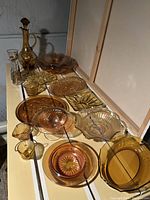 Full view of the collection showing a variety of amber glassware pieces arranged on a shelf including bowls, plates, and pitchers.