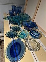 Shows full spread of blue and turquoise vintage glassware items including bowls, plates, goblets, and decorative pieces on a wooden surface.