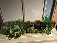 Full view of all vintage green glassware including bowls, pitchers, glasses, plate, and decorative pieces arranged on a shelf