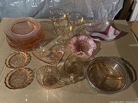 Full view of all pink glassware pieces arrayed on cardboard showing plates, bowls, goblets, decorative dishes