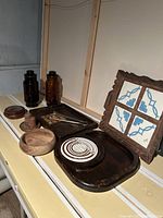 View of entire lot on shelf showing all items including cheese platters, bowl, salt and pepper shakers, brown glass canisters, and trinket holder