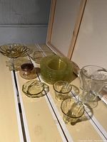Overview of set showing multiple yellow glass plates stacked, two yellow glass cups, small bowls and larger yellow decorative bowl, plus clear glass pitcher.