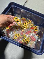 Bin filled with over 100 yellow NASCAR toy cars, many bagged individually, shown being held for size reference.