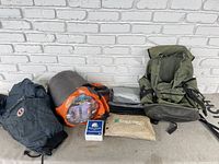 Full lot photo showing backpack, sleeping bag bag, rainwear bag, ration box, jacket, and tent bags.