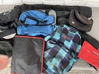 Overview of multiple carry bags including blue duffel, plaid Jansport backpack, and various small carry cases