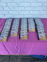 Forty-two unopened CD+G Karaoke Top Hits CDs spread and stacked on a purple cloth against a white brick wall background.