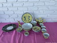 Full set displayed on pink cloth, showing all pieces including teapot, cups, bowls, plates and spoon holders with dragon pattern.
