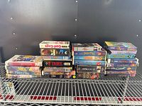 Photo showing a collection of VHS tapes stacked on a metal wire shelf, including Disney titles and other various movies.