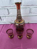 Full view of decanter and three glasses showing amber tint with gold tone horizontal stripes on decanter and gold rims on glasses.