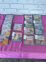 Multiple factory sealed karaoke and music CDs arranged on a purple fabric surface, including Top Hits Children's Songs series, Latin dance, and artist karaoke albums.