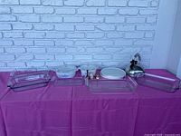 Full display of kitchen cookware lot including Pyrex baking dishes, CorningWare dishes, tea kettle, accessory items on purple cloth