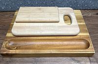 Three wooden cutting boards stacked showing different sizes, with the largest bottom board having a thick groove and wood grain variations.