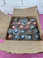 Box with 23 M&M branded yo-yos, each individually wrapped in plastic, showing alternating red and blue sides with white 'm' logos.