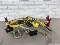 Full lot showing two bottle jacks, yellow tow straps, hand crank come along, and shackle on beige carpet against white brick wall