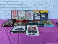 All 11 military board games displayed on a magenta cloth with a brick wall background, showing full box covers.