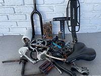 Wide shot of assorted bicycle parts including Schwinn book rack, front fork, cranks, pedals, seat and various gears laid out on surface