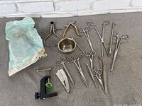 Full lot of miscellaneous clamps, scissors, tweezers, and small tools arranged on floor including packaged scissors.