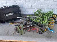 Wide shot of the handyman tool lot showing assorted metal hand tools including wrenches, ratchets, clamps, a black plastic carrying shelf, and coiled electrical cords.
