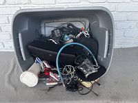 Large plastic tub filled with mixed electronics including cables, a white cylindrical device, and more