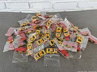 Overview of approximately 45 yellow and red Kellogg's Cornflakes toy cars individually bagged.