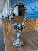Full view of the skeleton gothic style table mirror showing oval frame, skull and rose decorations, and ornate pedestal base.