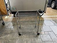 Front view of three-tier metal rolling cart with wire mesh shelves on caster wheels.
