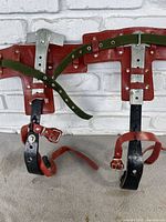 Overview of the pair of tree climbing pole shoe accessories, showing leather and metal build with green fabric straps.