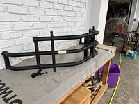 Metal cargo holder for truck bed tailgate placed on a workbench, showing side angle with tubular metal construction and mounting clamps.