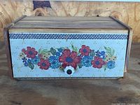 Front view of vintage wooden breadbox showing colorful floral painted design on front panel with knob handle.