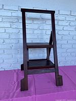 Front view of the wooden two-step fold-down stepstool showing slatted step surfaces and stable frame.