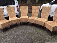Six high back chairs in a row showing the overall set and shape with jute woven seats and backs and wooden legs.